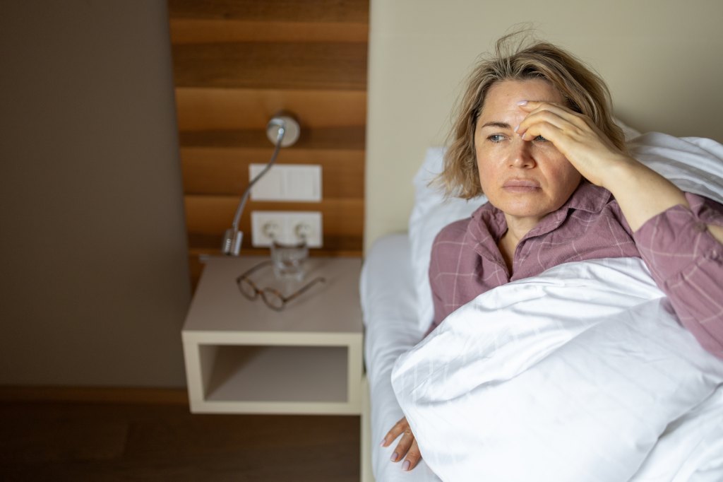 Sick mature woman suffering from flu and headache while lying in bed at home