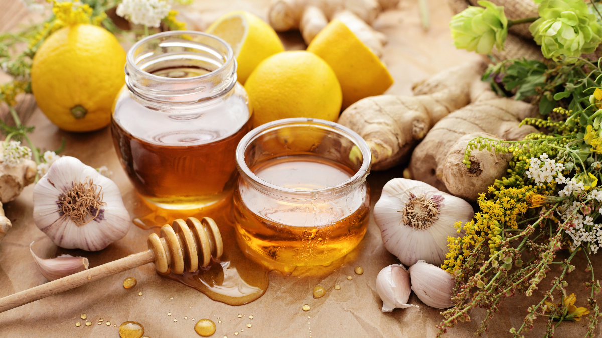 A jar honey beside garlic, which have health benefits, along with ginger and lemons on craft paper