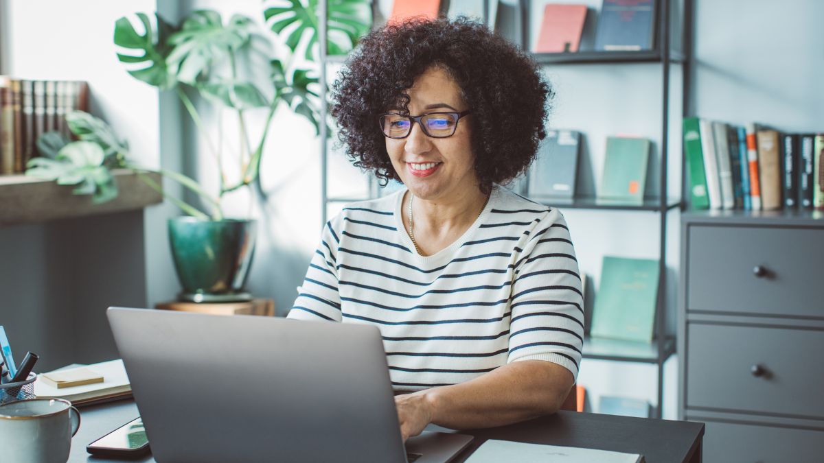 woman wearing glasses smiling while working on computer figuring out how to make money from hobbies