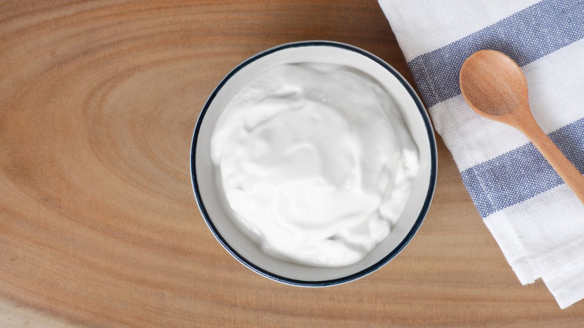 bowl of plain yogurt on wooden table with spoon, which can be used to treat oral thrush