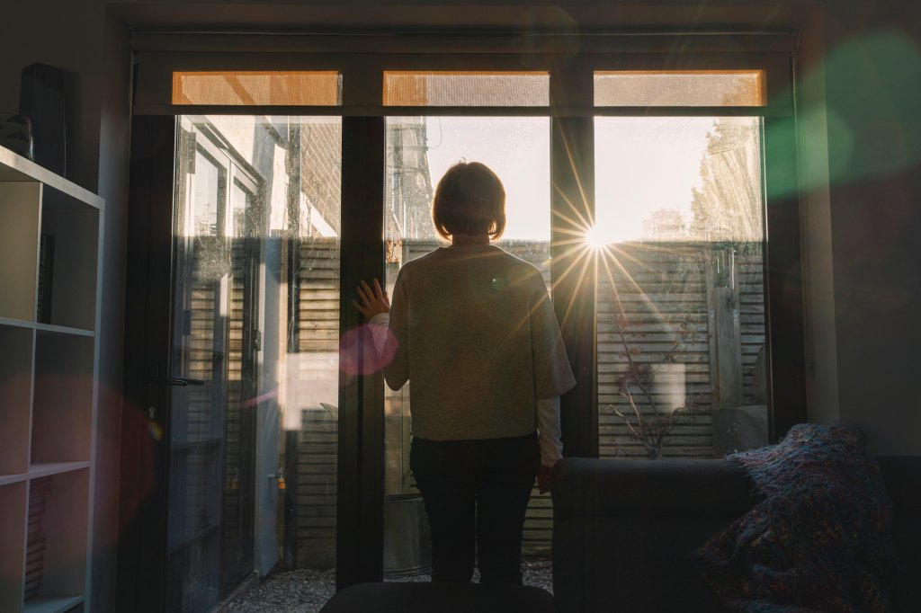 mature woman looking outside window at sun down