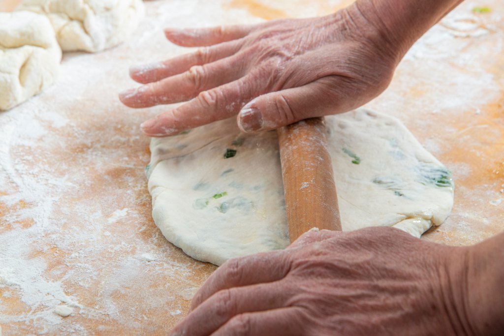 woman rolling out dough to make scallion pancakes on floured surface