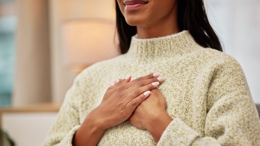 Closeup of a woman holding her chest while breathing for calm, peace and zen mindset for meditation. Breathe, relax and zoom of a female person hands on her heart for grateful gesture in living room.