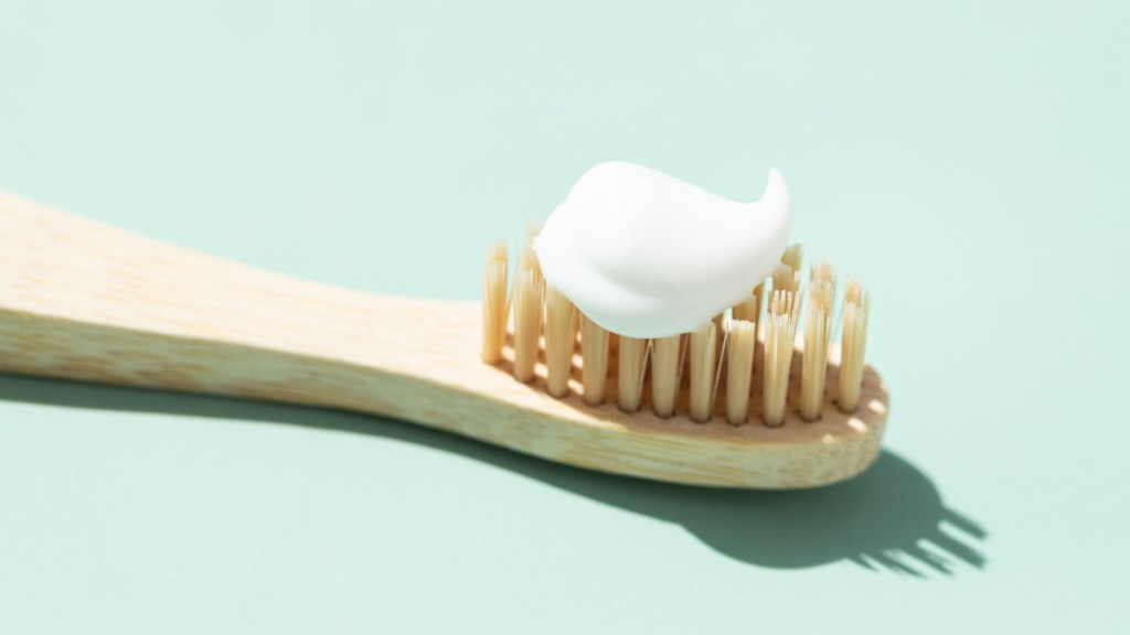 A close up of a bamboo toothbrush on a mint-colored background with toothpaste, which helps stop trouble for folks wondering how to stop bleeding gums
