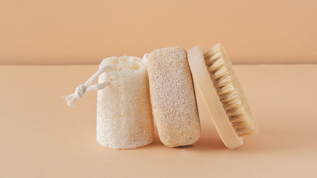 a coarse loofah, pumice stone and body brush on a peachy-colored background