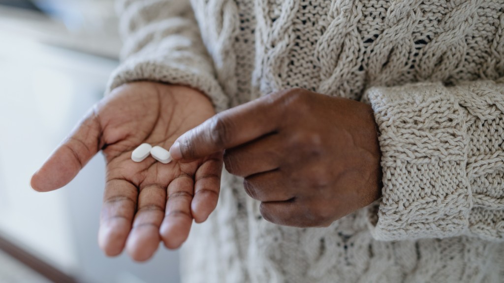 A close up of a woman in a sweater holding two white pills, which can help relieve sinus pressure in ears