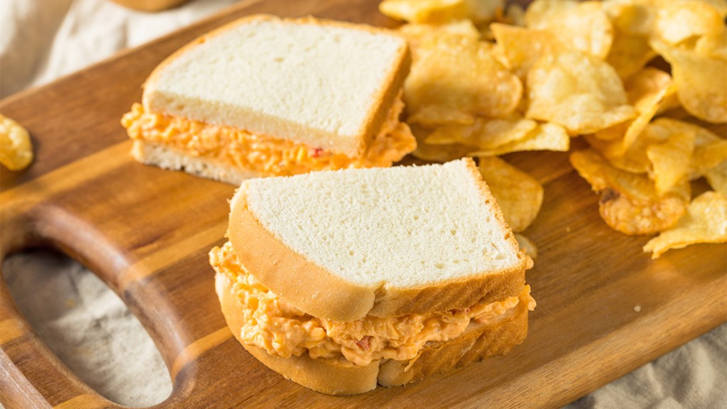 A pimento cheese sandwich on a board with chips