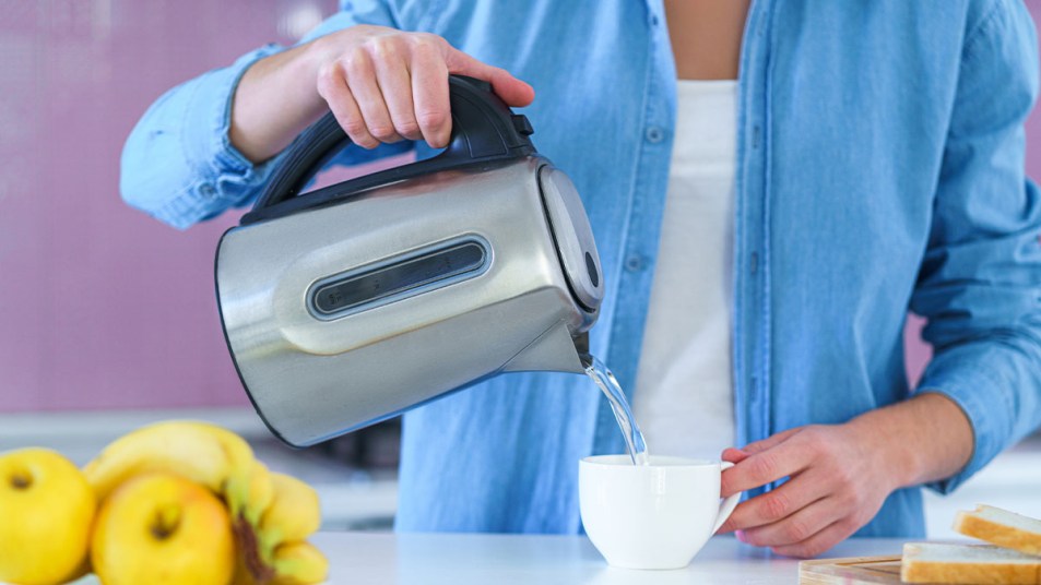Woman pouring hot water into a mug from a clean electric kettle