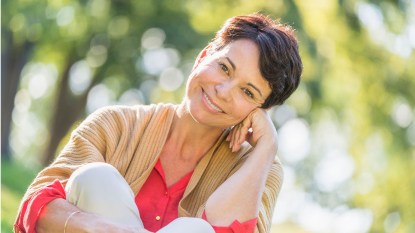 Happy older woman sitting outside as result of healthy aging tips