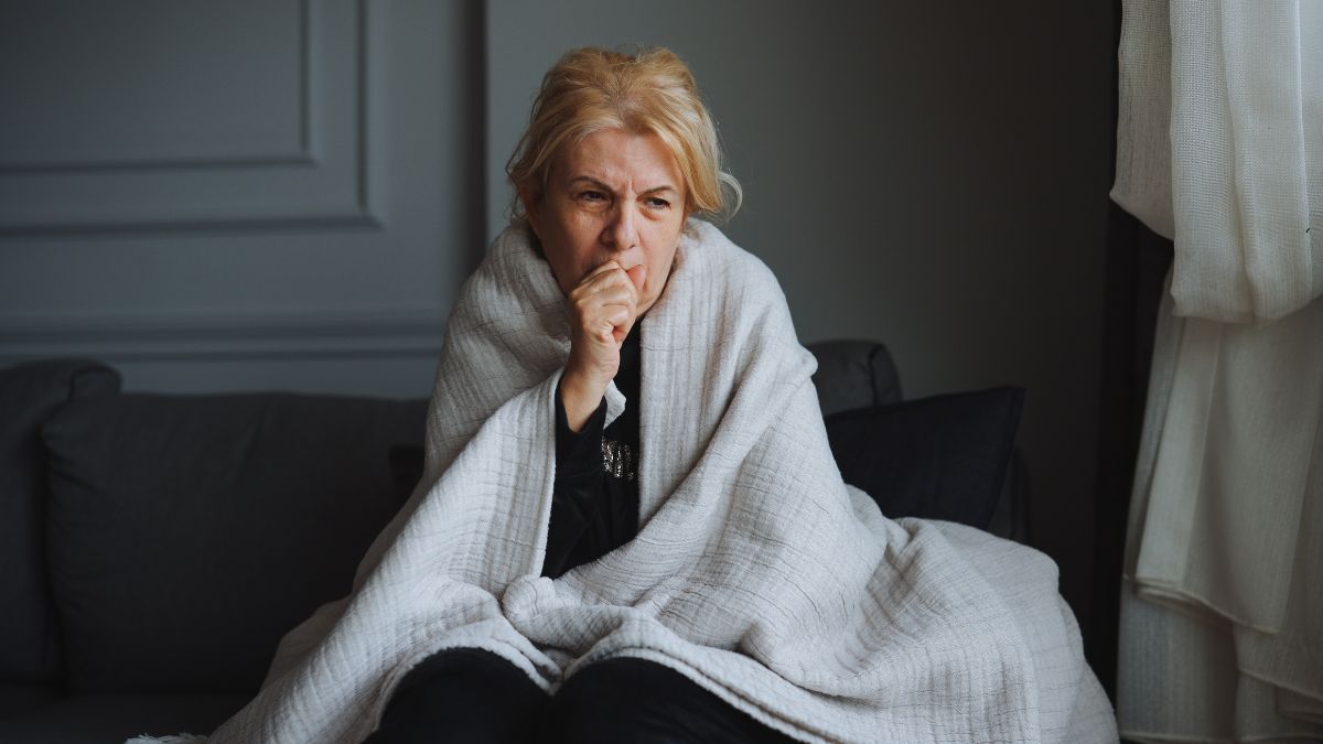 woman sitting on cough wearing blanket coughing wondering "can the flu turn into pneumonia?"