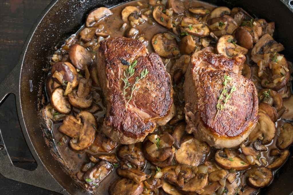 pan-seared filet mignon sitting in creamy mushroom sauce in cast iron pan