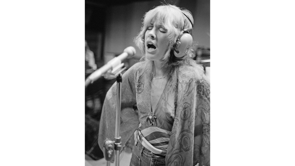 Stevie Nicks singing in studio with flare sleeve shirt and jeans