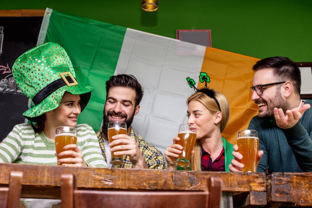 Four good friend talking and drinking beer in pub with Irish flag on background and smile