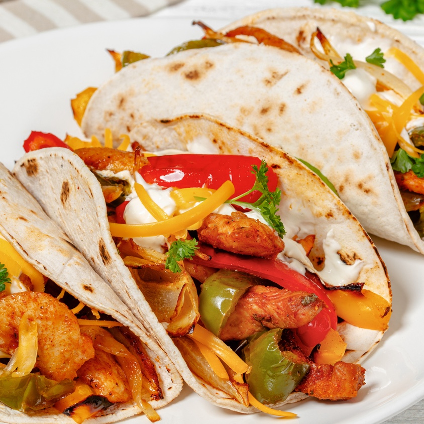 Sheet pan chicken fajitas served on tortillas with sour cream and cheddar cheese