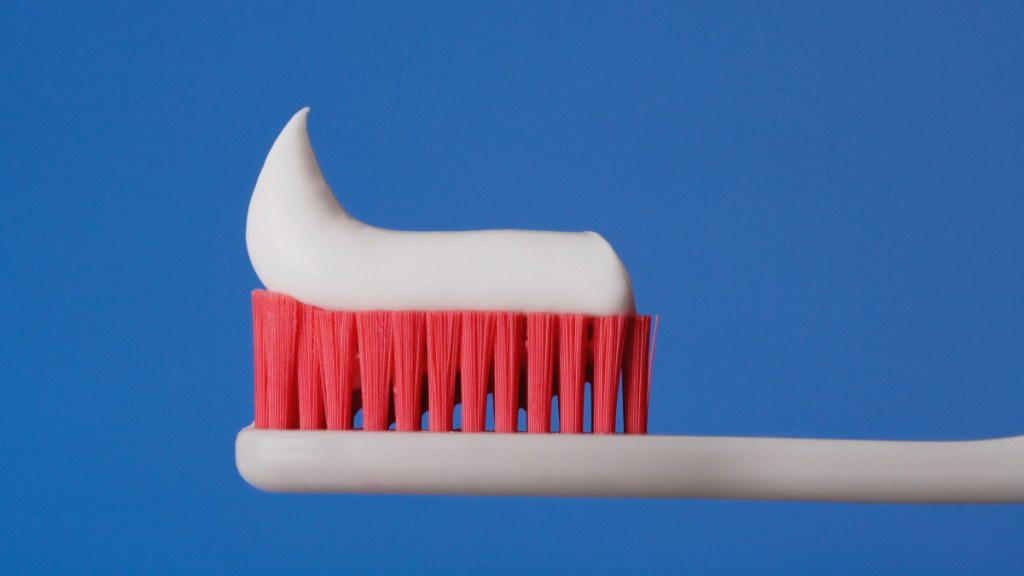 A wooden toothbrush with red bristles and white toothpaste against a blue background