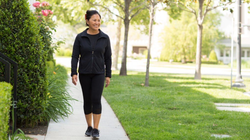 A woman in black gym clothes walking on a sidewalk near greenery