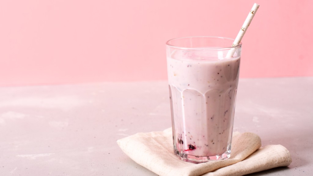 A berry smoothie with a straw on a napkin against a pink background