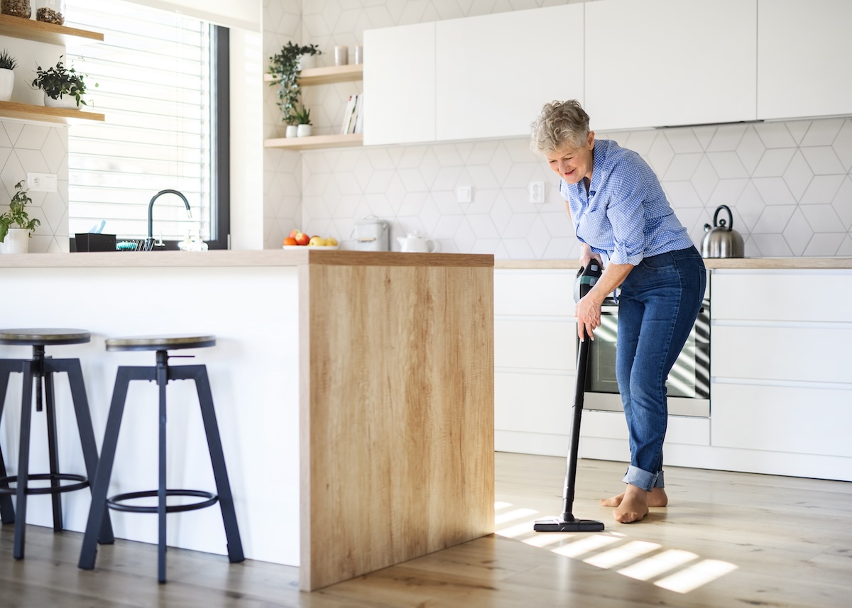 A senior woman with vacuum cleaner indoors at home, cleaning kitchen