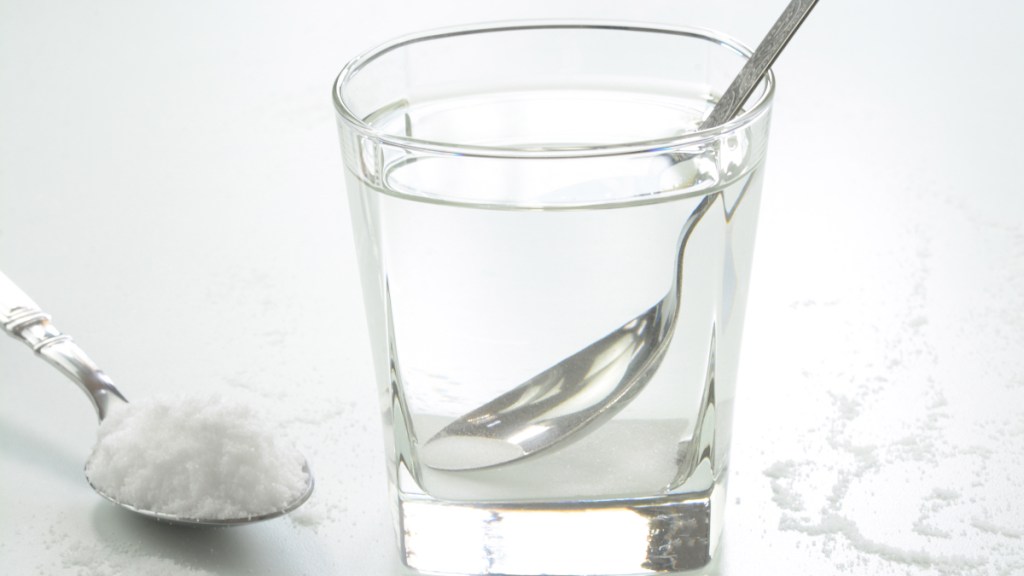 A glass of water beside a spoon of sale, which helps get rid of canker sores fast