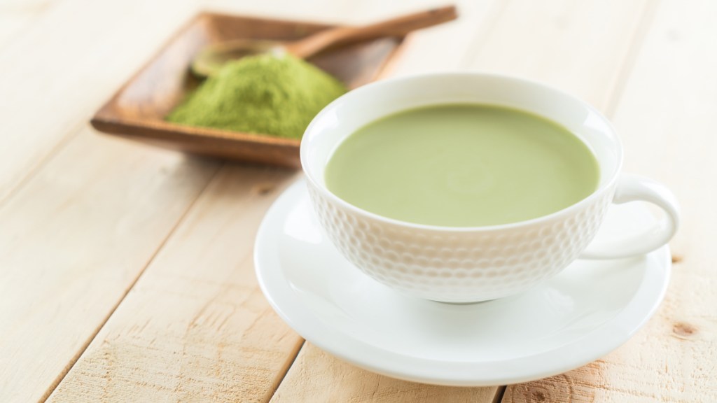 A white mug filled with matcha tea beside green matcha powder