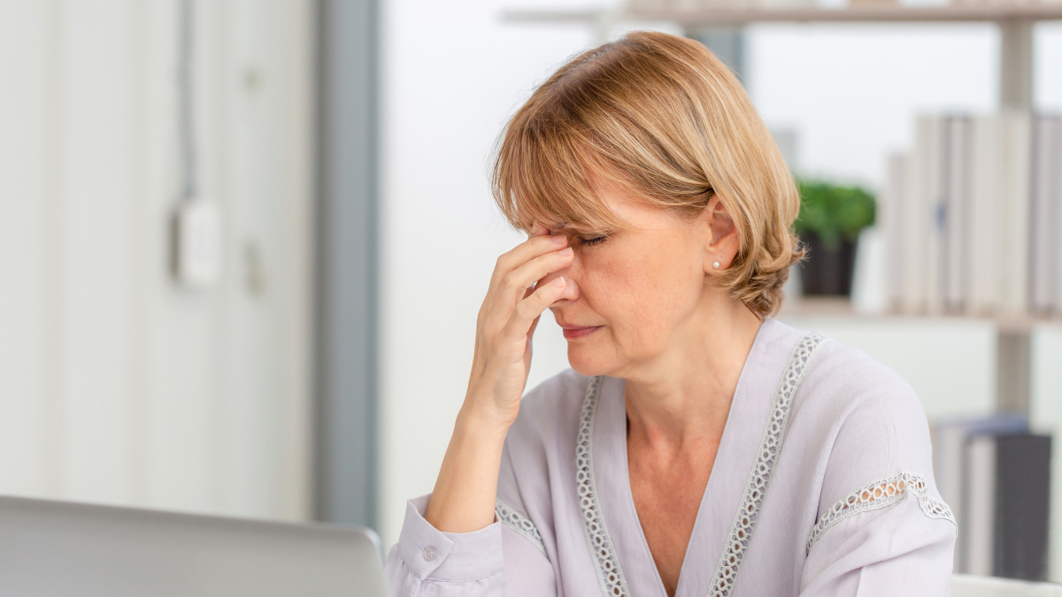 A woman with short blonde hair pinching the bridge of her nose due to fatigue caused by iron deficiency without anemia