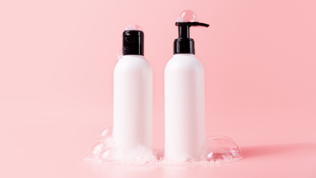 White shampoo and conditioner bottles against a pink background