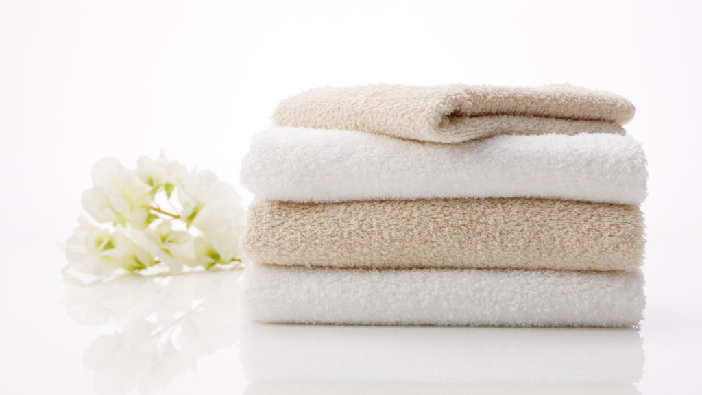 A stack of white and tan washcloths beside a white flower