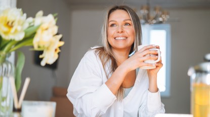 A woman in a white top holding a mug, drinking tea for allergies