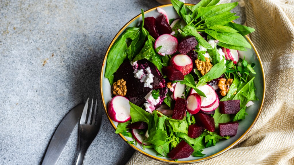 A bowl of spinach, beets and radishes on a stone countertop