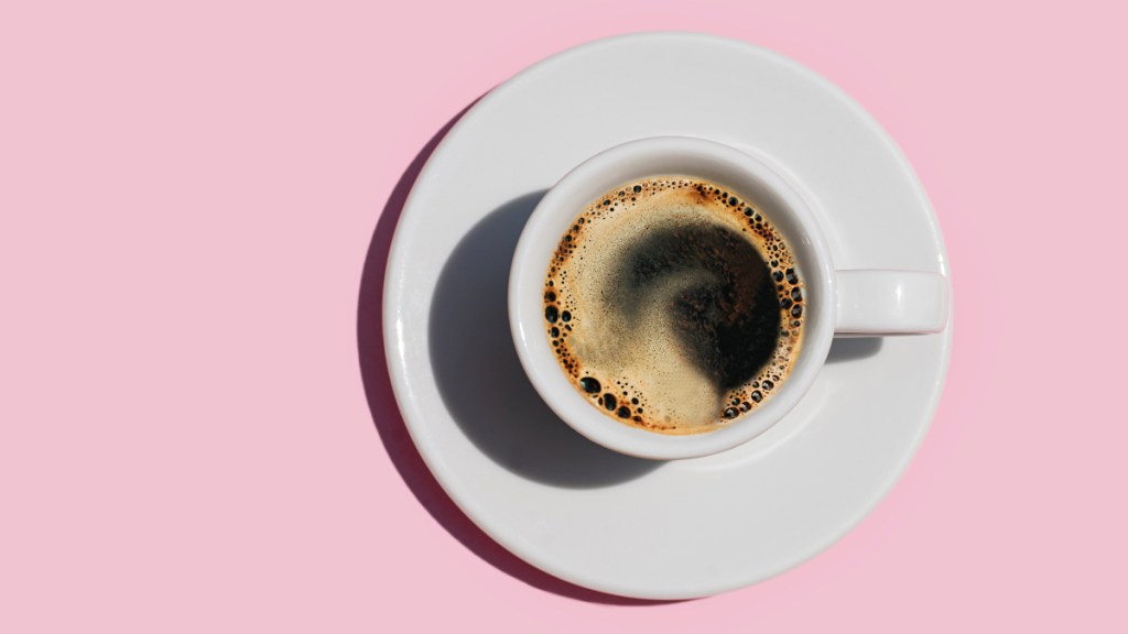 A cup of coffee in a white mug on a pink background