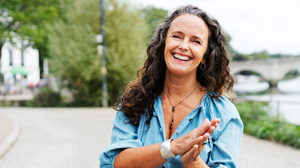 A woman with dark hair smiling and holding her hands together now that she's learned how to reduce cortisol