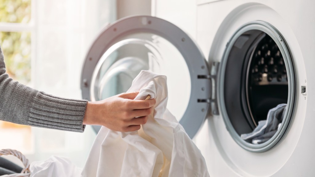 A close-up of a woman putting sheets in the washing machine to reduce norovirus risk