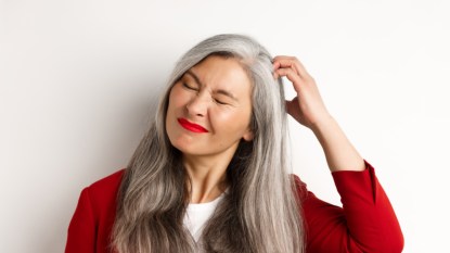 A woman with an itchy scalp and hair loss scratching her head with her eyes closed