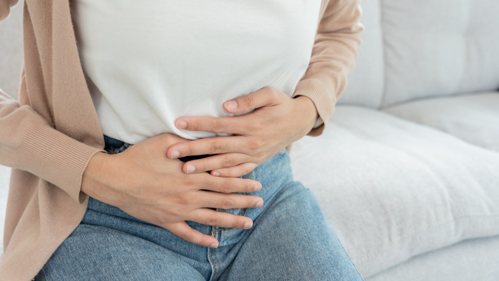 A close up of a woman in jeans and white top with her hands touching her stomach