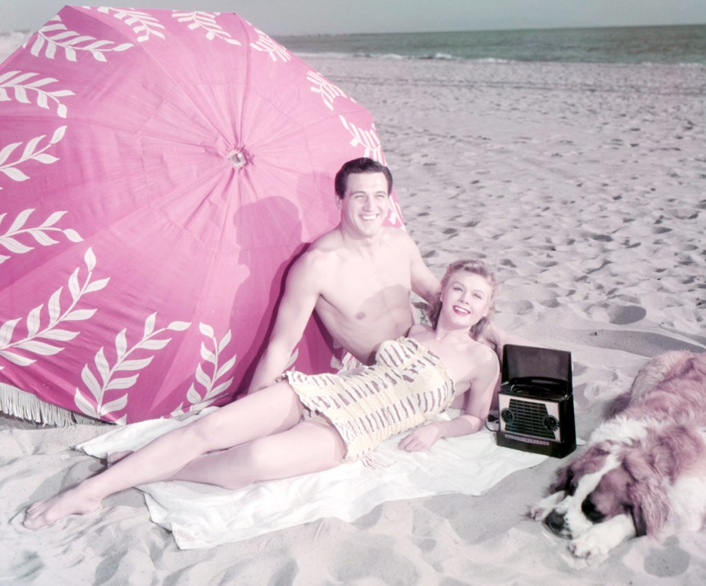 American actors Rock Hudson (1925 - 1985) and Vera-Ellen (1921 - 1981) on a beach with  a dog, circa 1955
