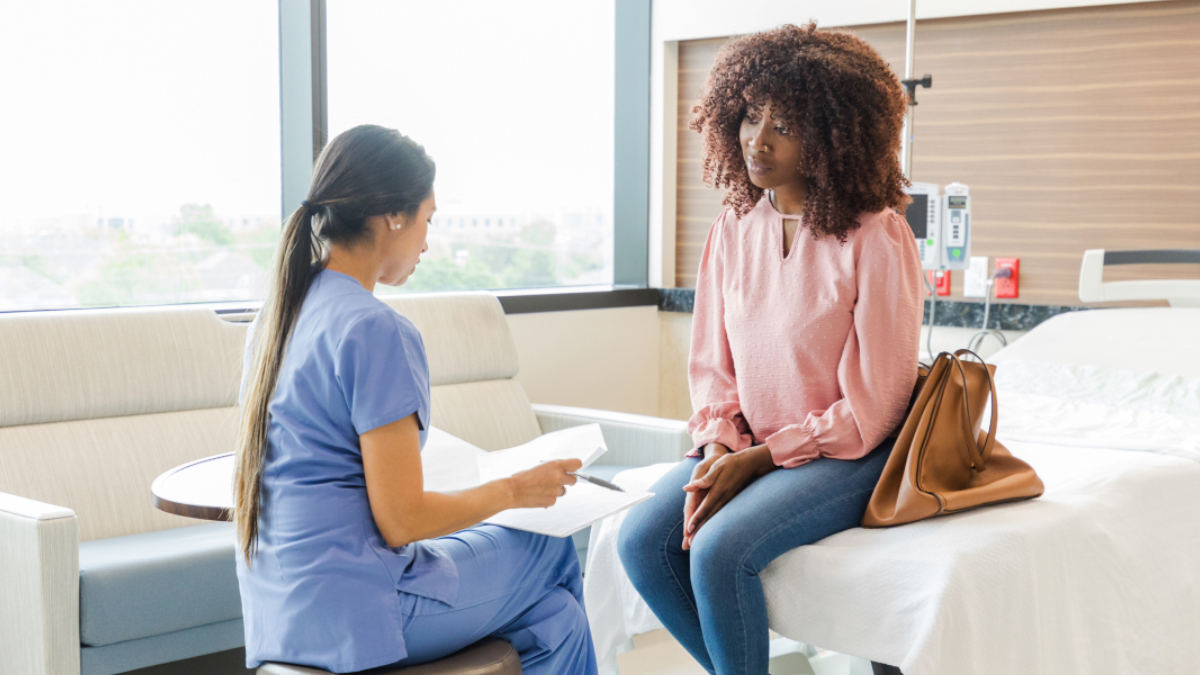 A woman sitting on a hospital bed talking to a doctor in scrubs about how long you are contagious with norovirus