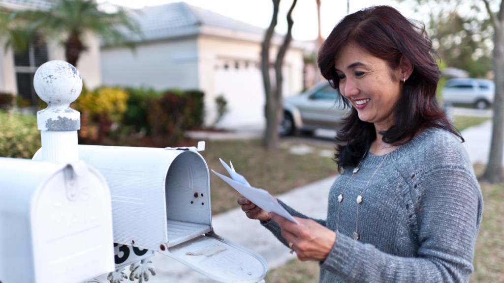 A woman with dark hair checking her mail at a white mailbox