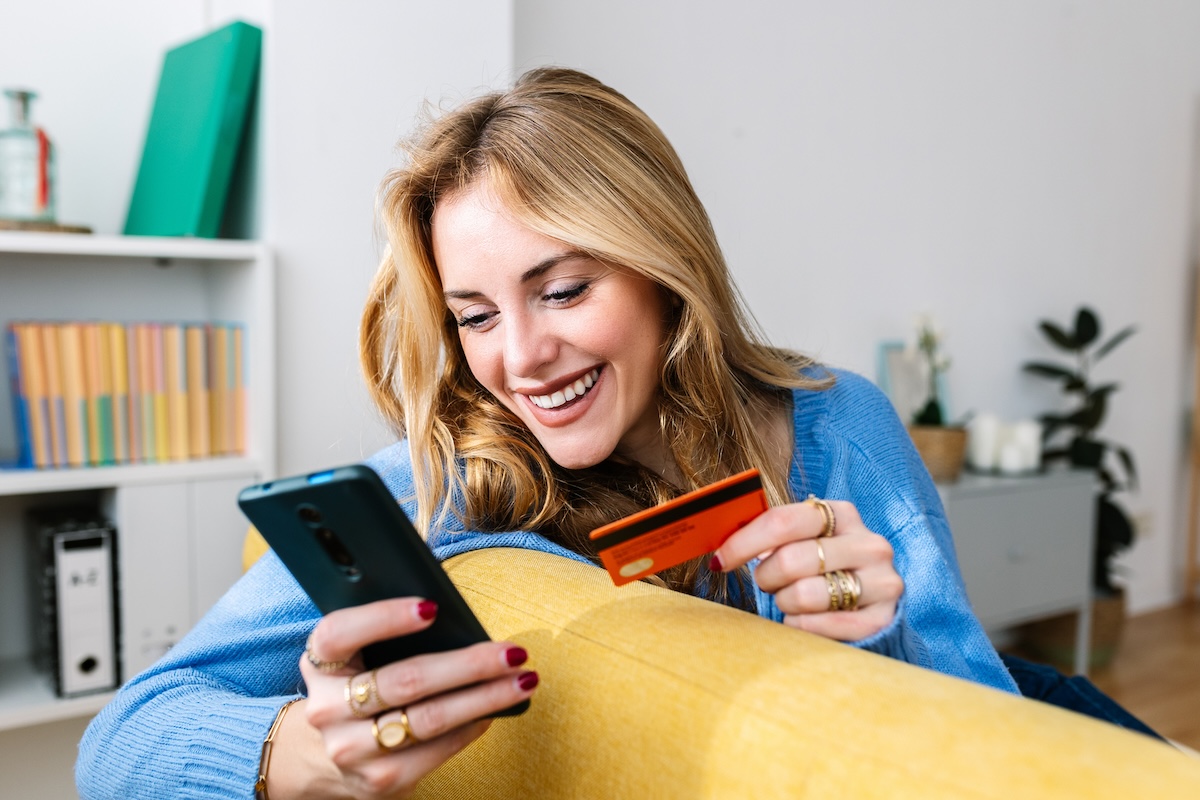Happy young woman holding credit card while shopping online at home