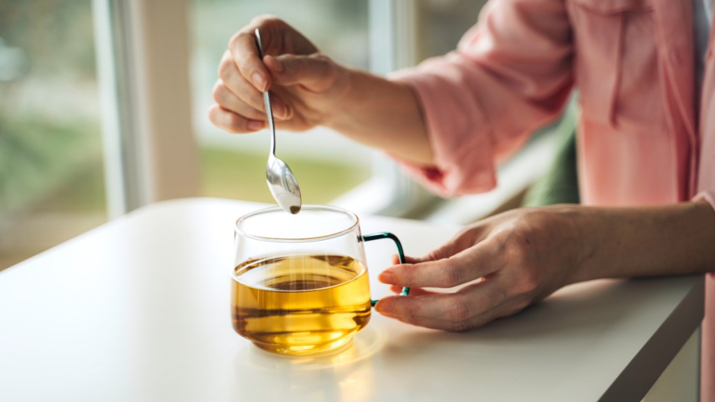 A close-up of a woman stirring a cup of green tea for allergies