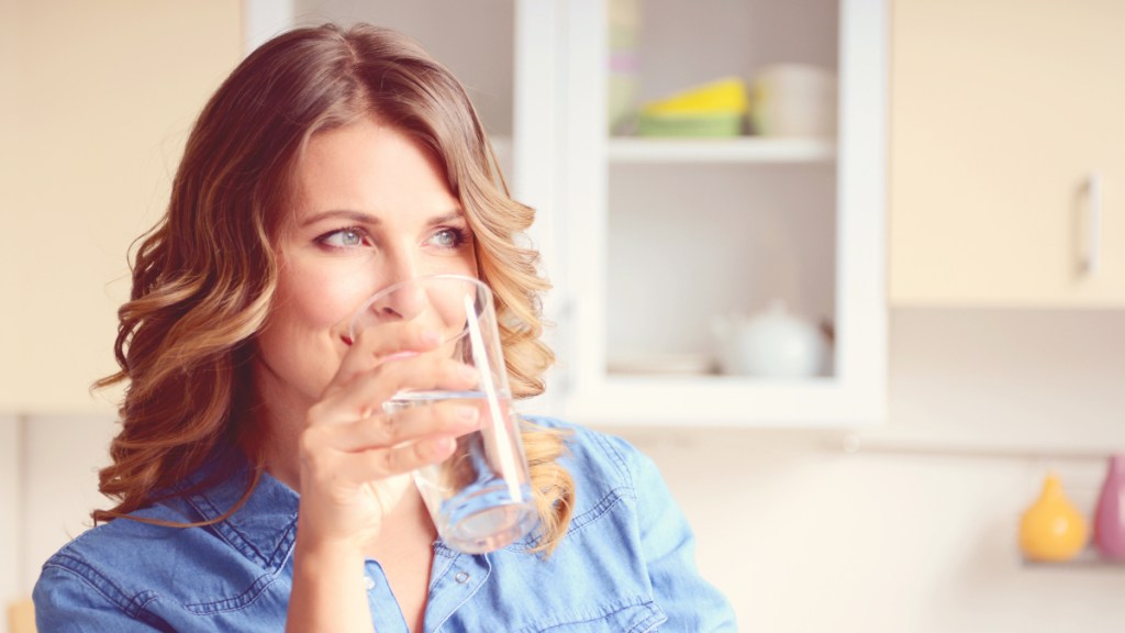A woman in a chambray top drinking a cup of water with Epsom salt for constipation