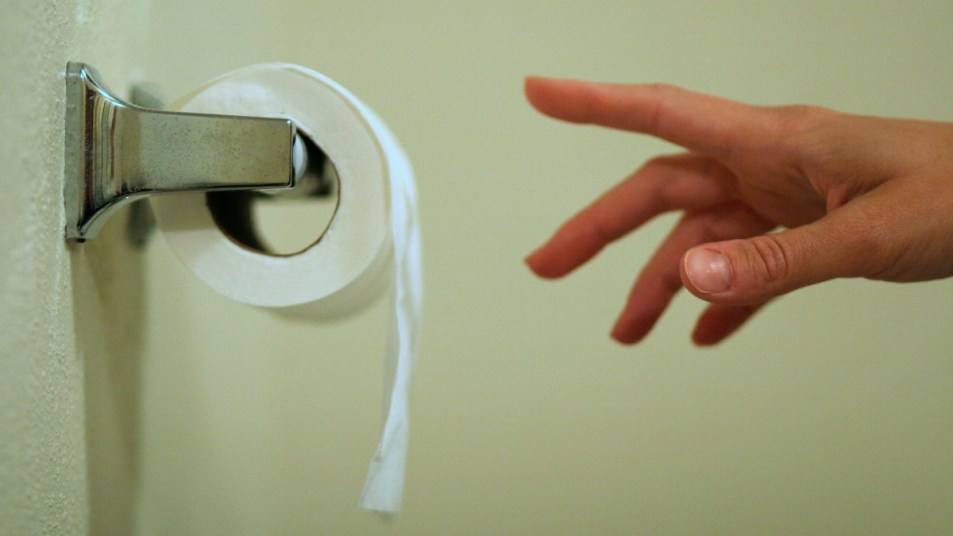 A close up of a woman's hand reaching for a roll of toilet paper due to urine that smells like popcorn