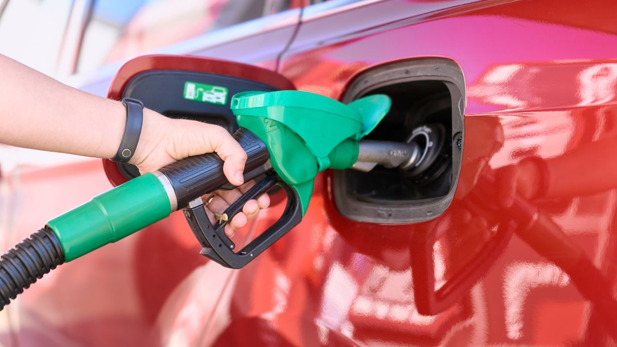 Close-up of a woman standing at a gas station filling her car with gasoline.