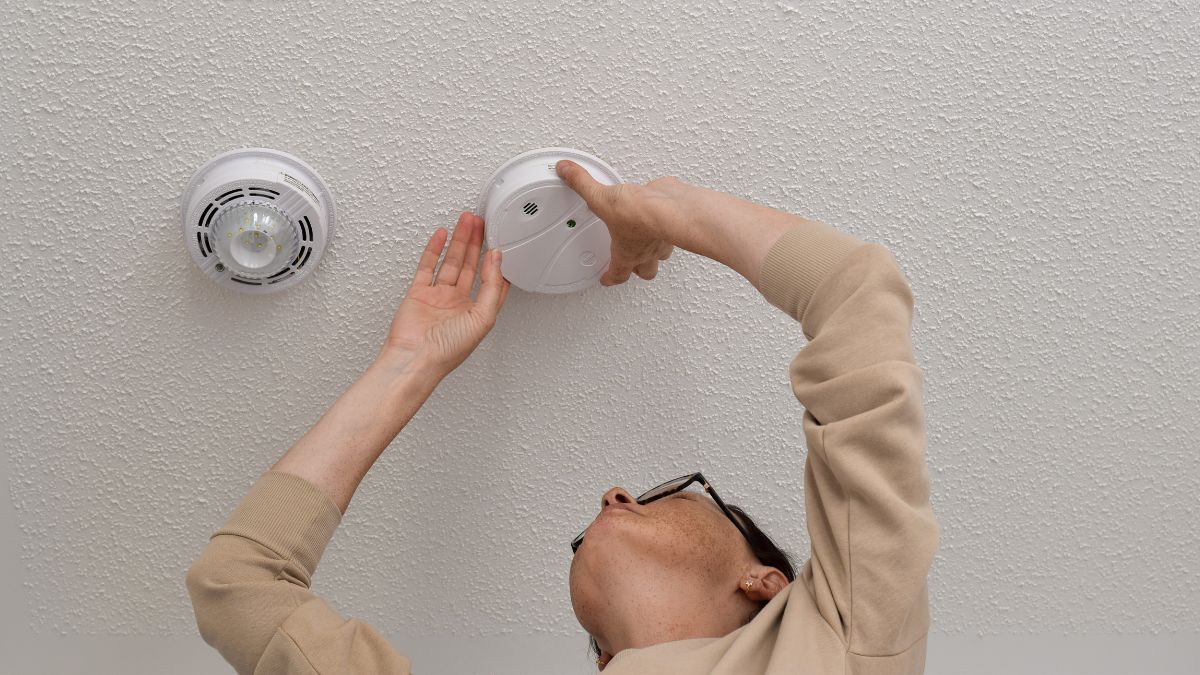 woman learned about home maintenance cost-saving tips and is checking fire alarm