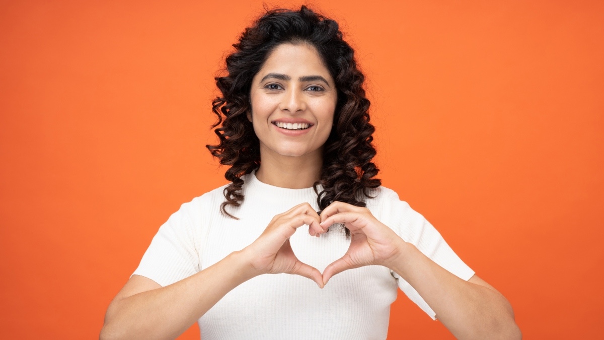 A healthy woman making a heart with her hands against an orange background