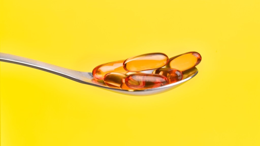 A spoonful of omega 3 fish oil capsules, which should be taken each day, against a yellow background