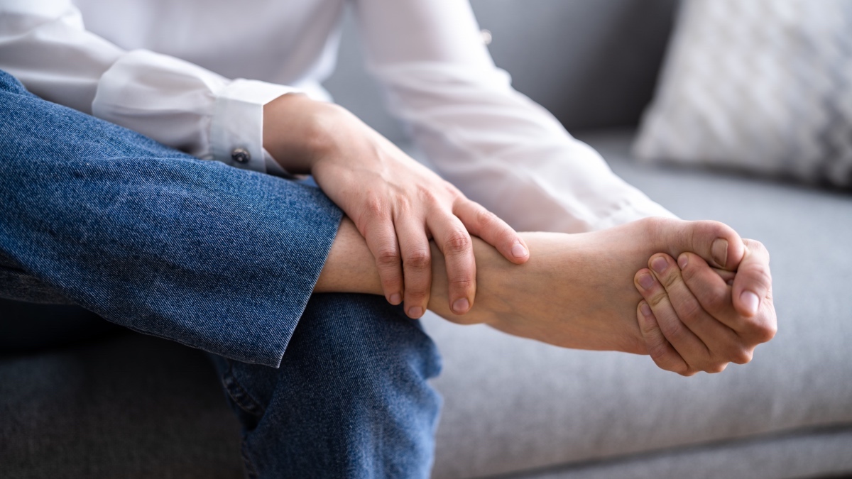A close-up of a woman's hand touching her foot, which has a tailor's bunion
