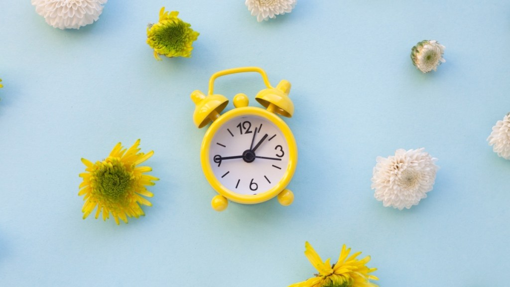 A yellow alarm clock on a blue background with yellow and white flowers