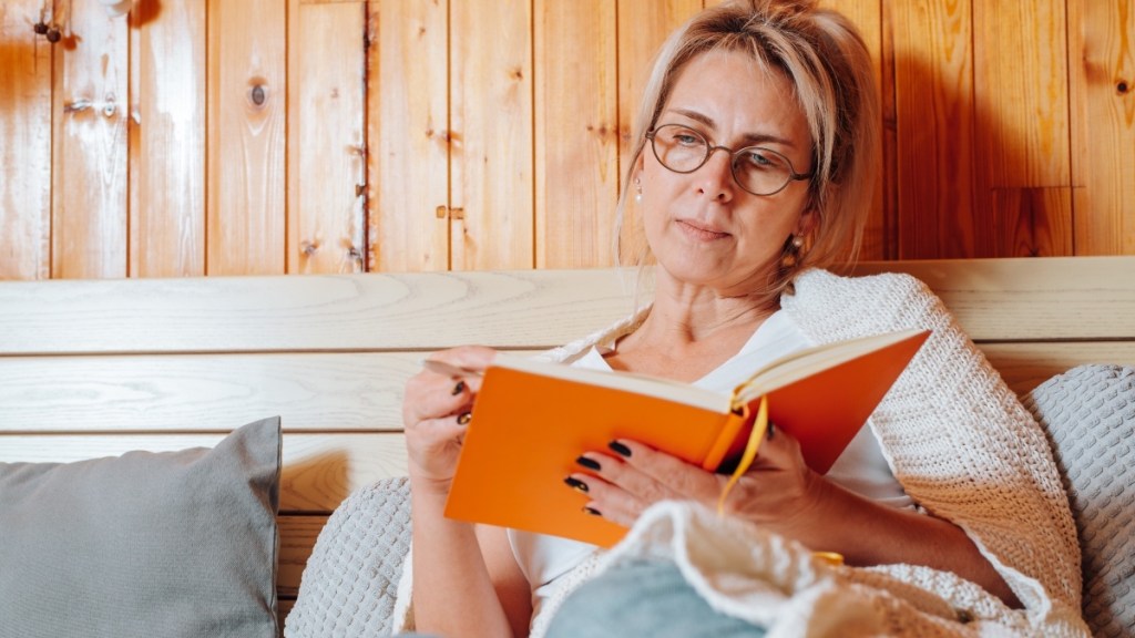 A woman sitting in bed writing in an orange journal to avoid waking up dizzy