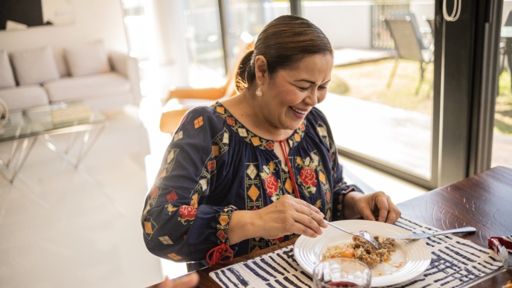 A woman sitting at her dining room table smiling while putting food on her plate