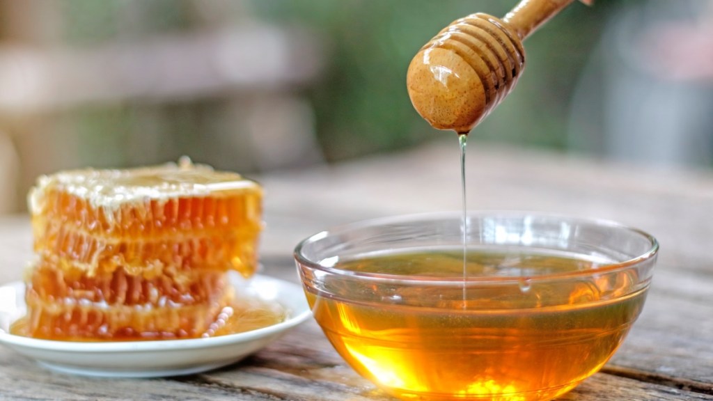 A stack of honeycombs beside a bowl of honey, a gut-friendly sweetener, with a wooden dipper